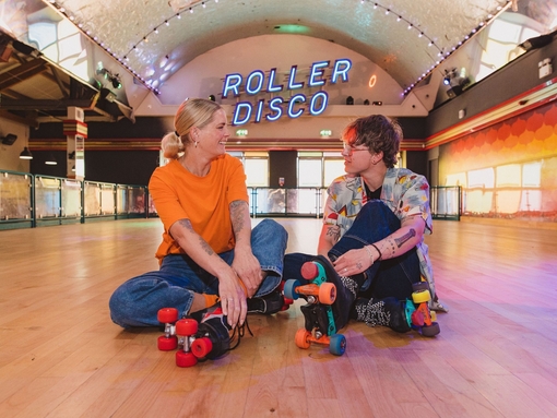 A woman and a man sit wearing roller skates at a Roller Disco